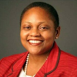 About Us 7 Jendayi Frazer smiling in professional attire, wearing a red blazer and pearl necklace.
