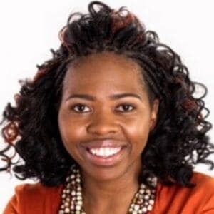 About Us 17 African woman with curly hair smiling, wearing traditional clothing and jewelry.