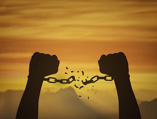 Silhouette of broken shackles held by raised fists at sunset.