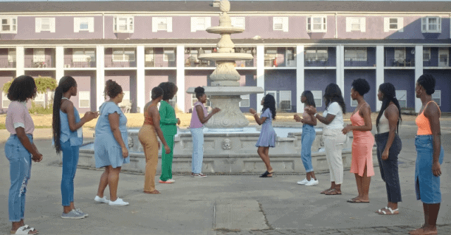 People standing in a circle near a fountain, engaging in a social activity outdoors.