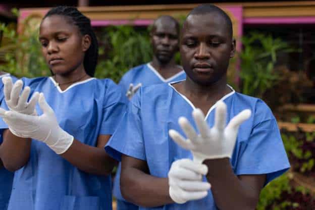 Nigerian healthcare workers preparing for a medical ceremony, wearing blue scrubs and gloves.