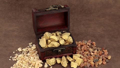 Gold nuggets spilling from an open wooden chest on a brown surface.
