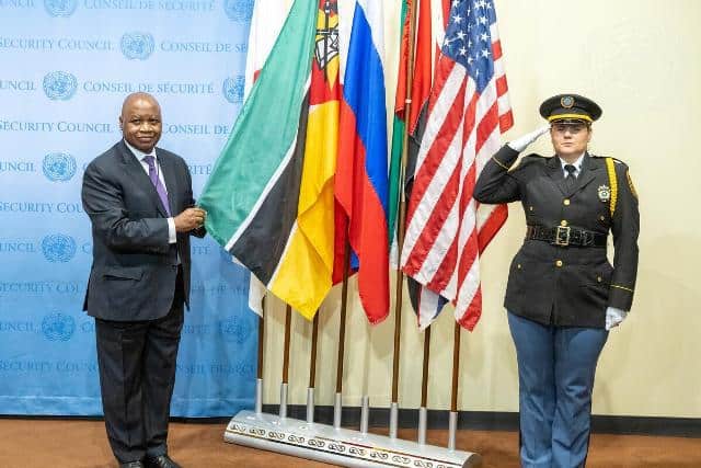 Diplomat and police officer standing beside flags at international security event.