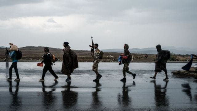 Group of people walking across a wet landscape with cloudy sky background.