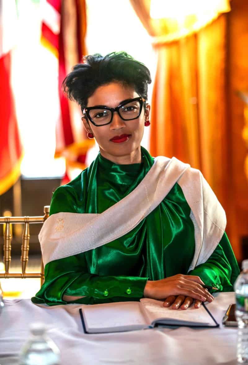 African woman in stylish green and white attire with glasses at a cultural event.