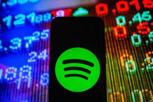 Smartphone displaying Spotify app against colorful stock market data background.
