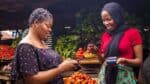 Two women using smartphones at an outdoor market in Africa.