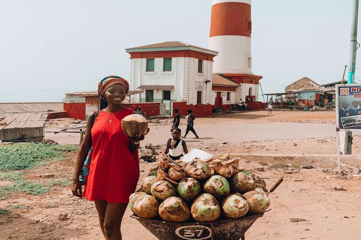 Local woman selling coconuts near lighthouse in Mozambique, vibrant coastal scene.