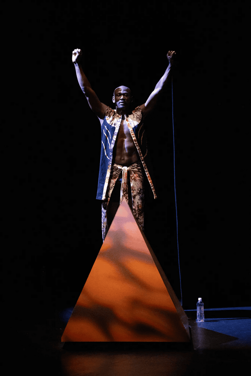 African performer on stage with arms raised in a dramatic pose.