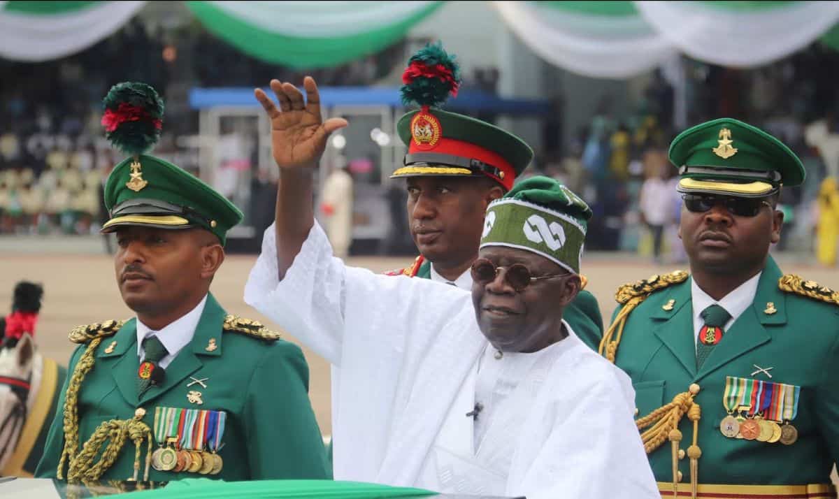 President in traditional attire with military officials at a public event.