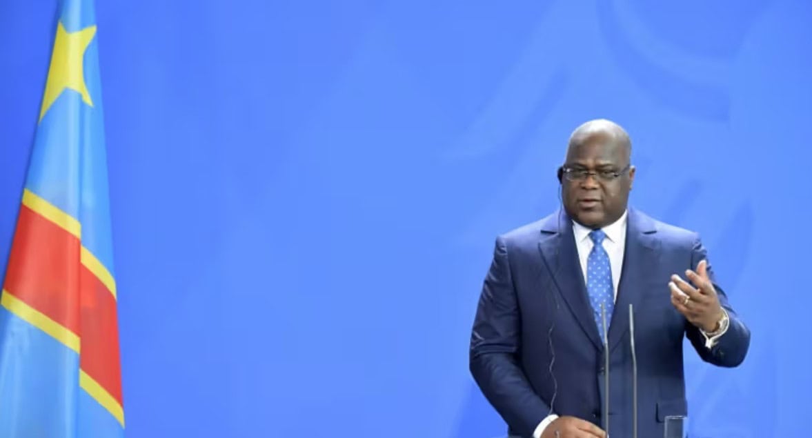 Man speaking at a press conference with Mozambique flag in background.