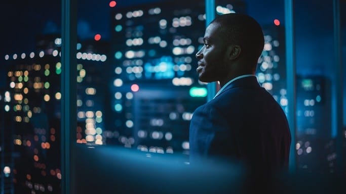 African executive contemplating innovation amidst city skyline lights.