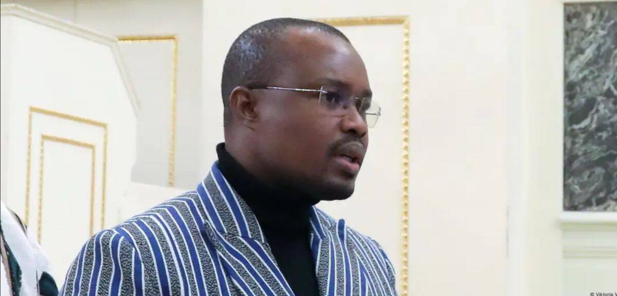 African man wearing a striped suit and glasses at an indoor event.