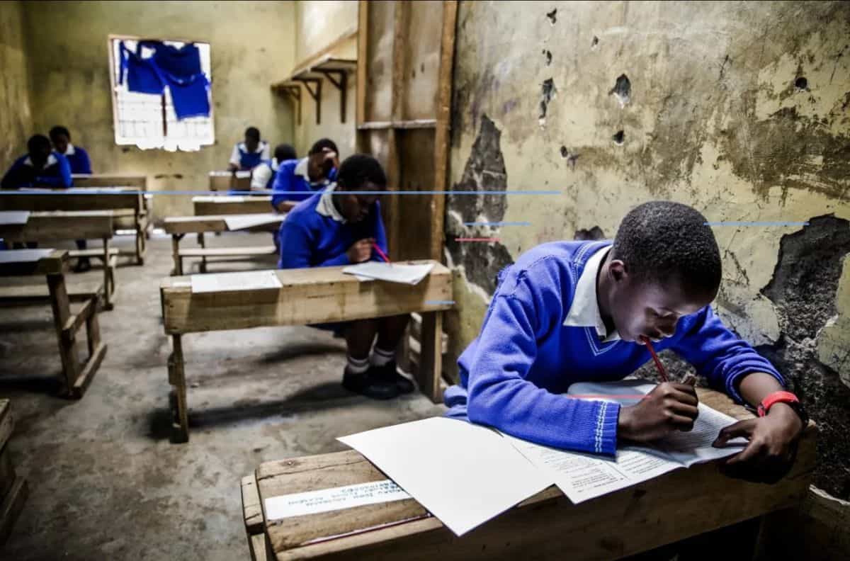 School children in Kenya studying in a classroom with worn walls and wooden desks.