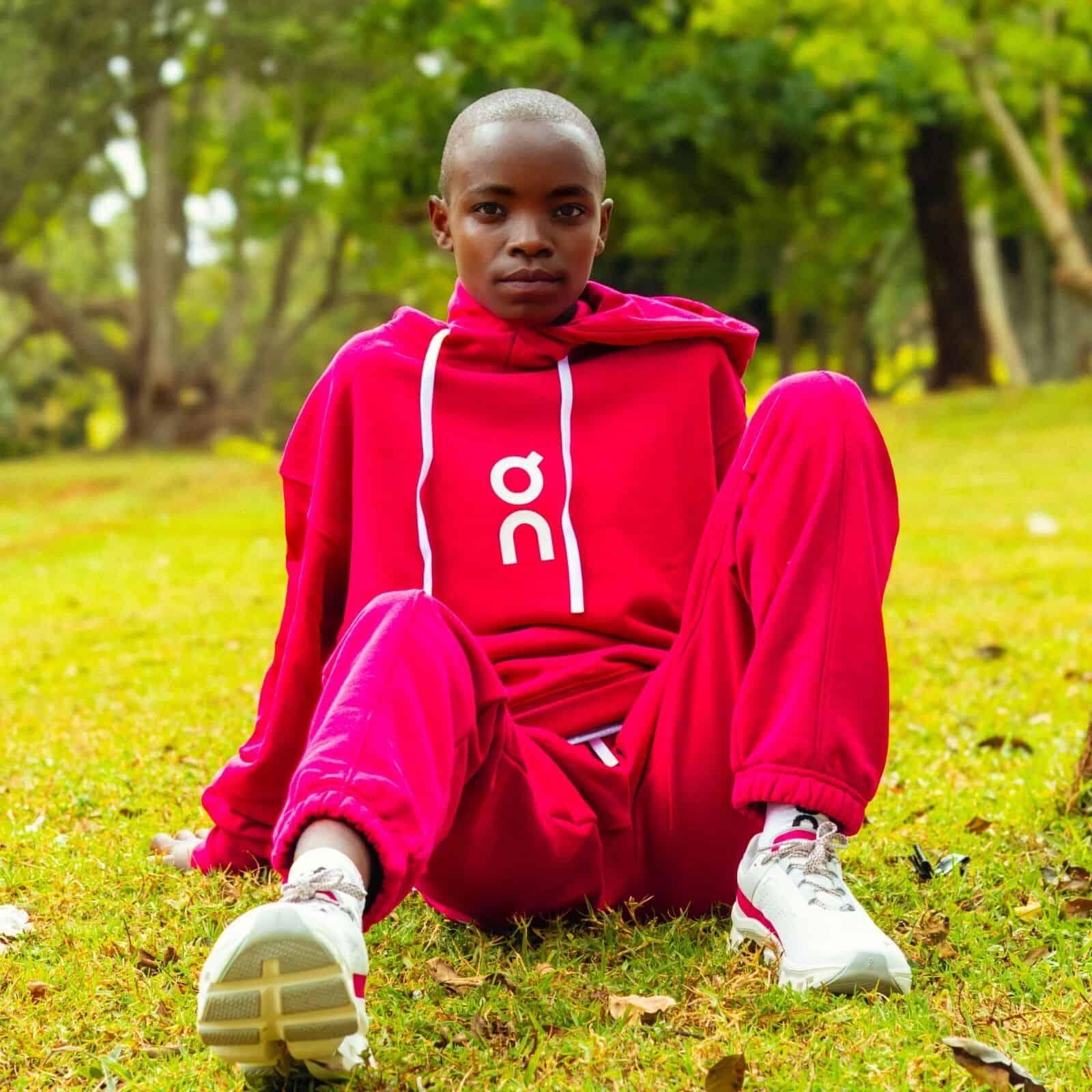 Young female athlete in red sportswear sitting outdoors on grass, ready for running.
