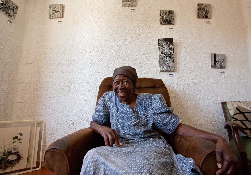 Elderly woman smiling in a community art space, showcasing local creativity and cultural expression.