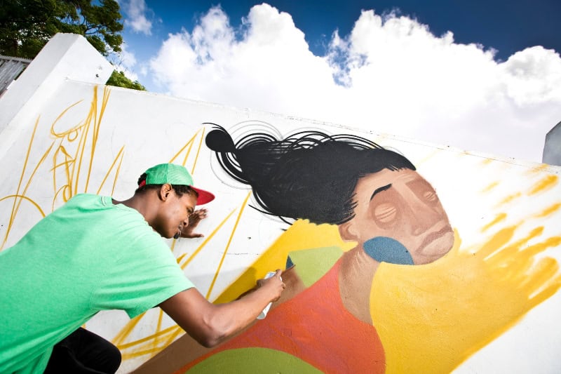 Young artist painting a vibrant mural on a community wall in a township setting.
