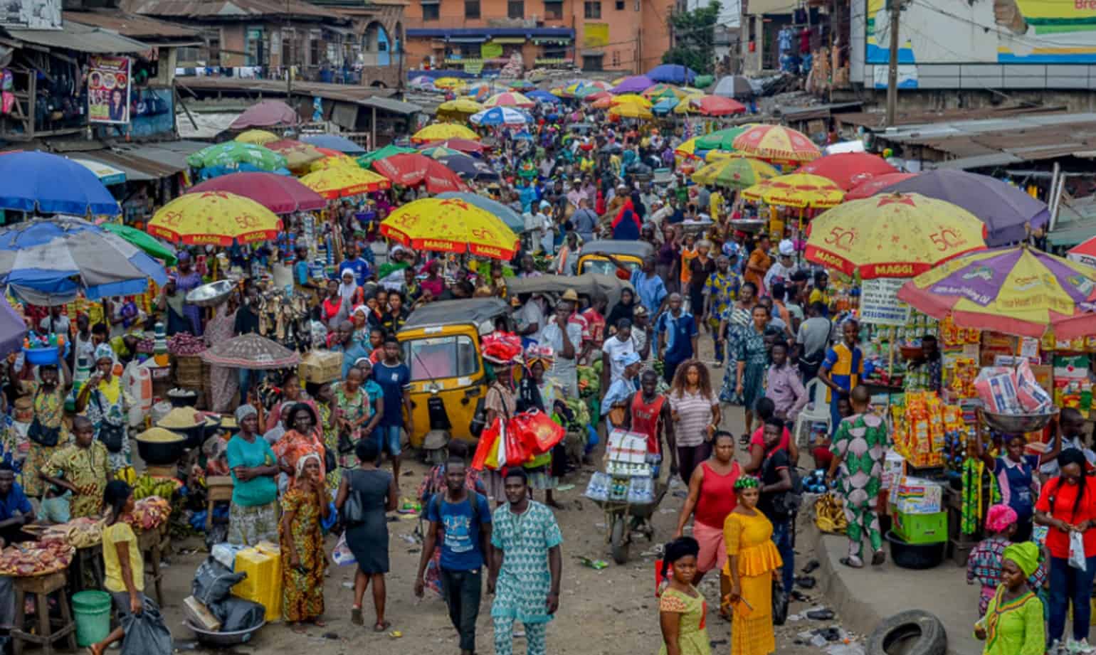 Colorful market with vendors and shoppers under umbrellas in Africa.