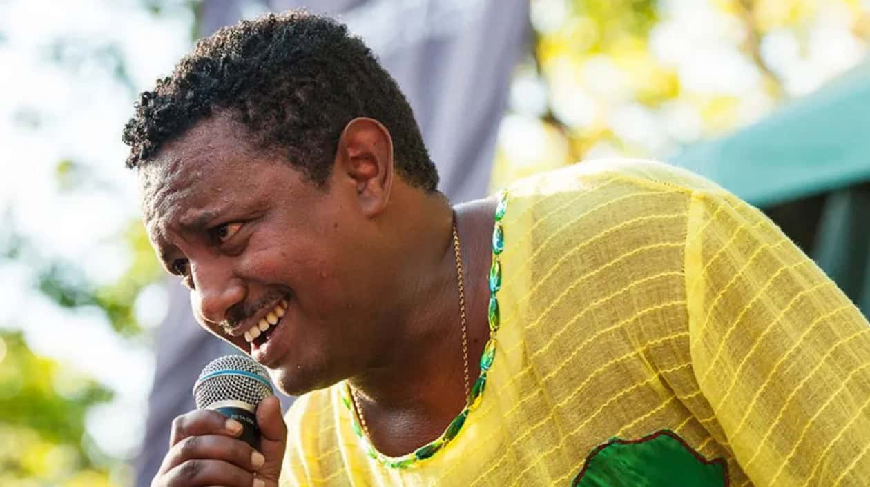 African man singing into a microphone at outdoor event.