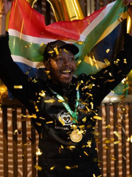 An African Barista On An Extraordinary Journey 1 African barista celebrating victory with flag and medals.