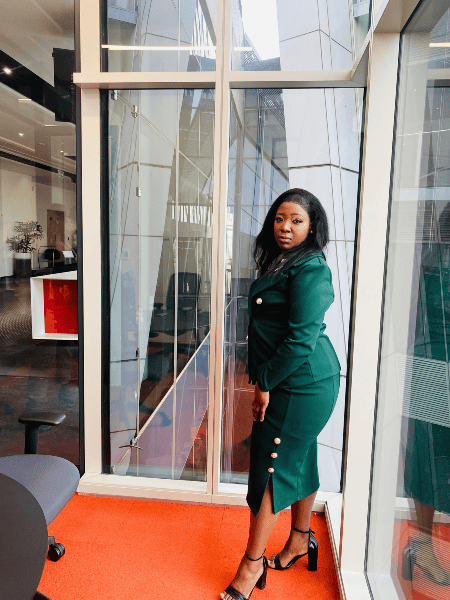 Woman in business attire standing by glass window in modern office.