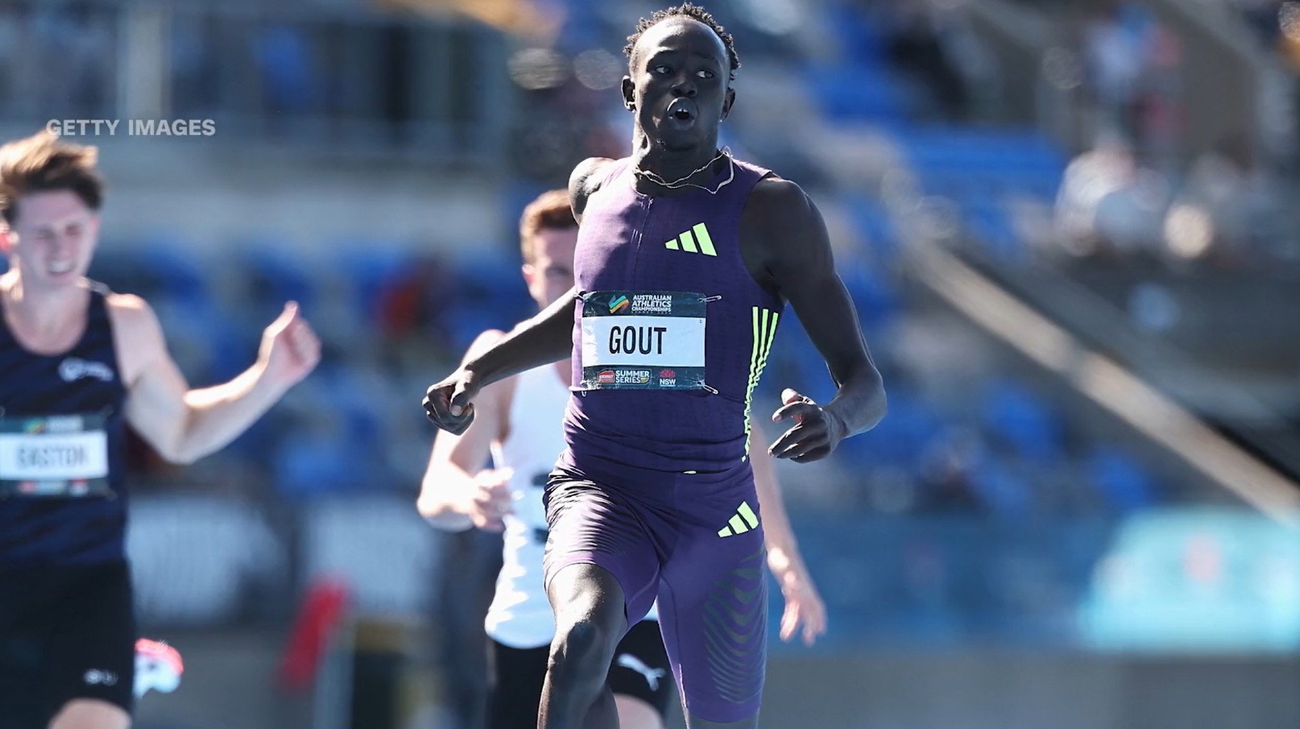 Athlete running on a track during a race, wearing a purple sports outfit with "GOUT" on the bib, foc.