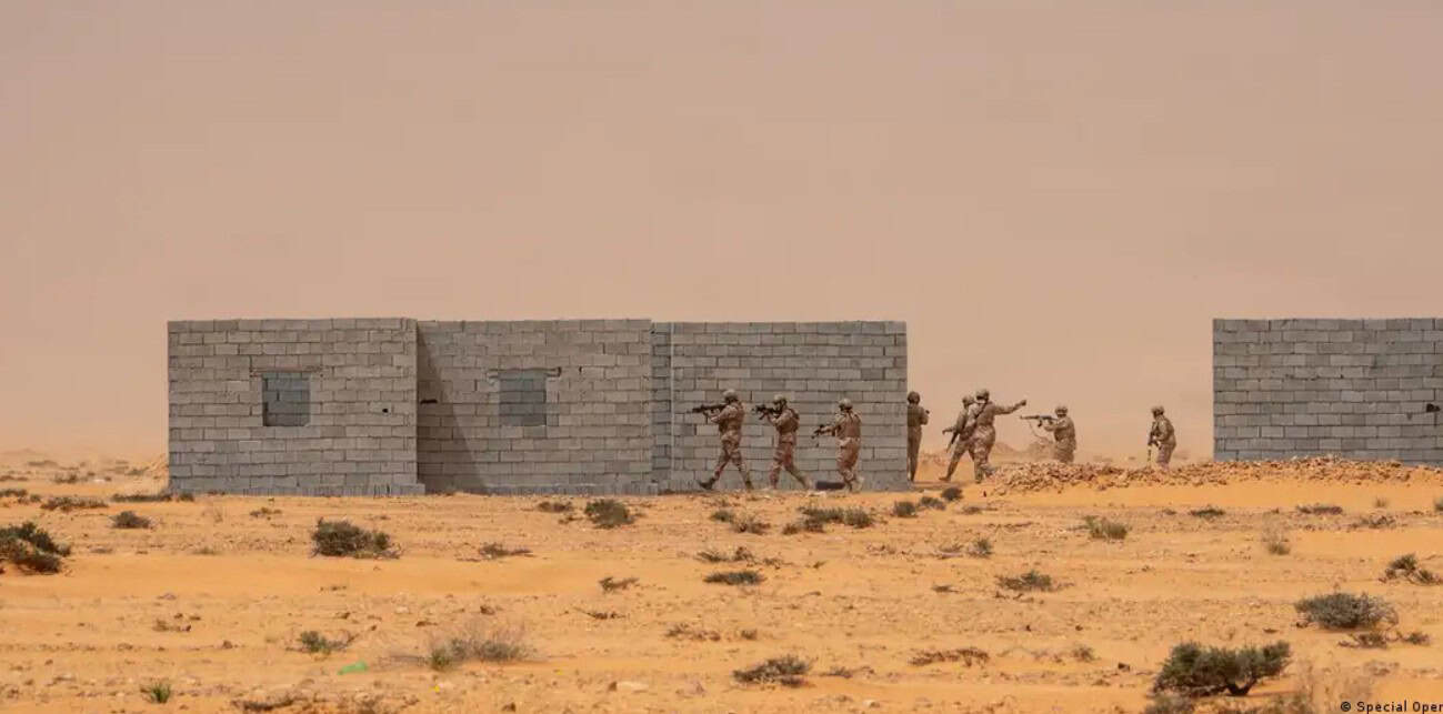 Soldiers marching past a building in a desert landscape in Africa.