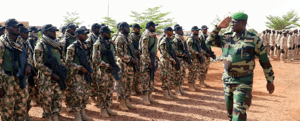 Soldiers in camouflage gear listening to a commanding officer in an outdoor setting.