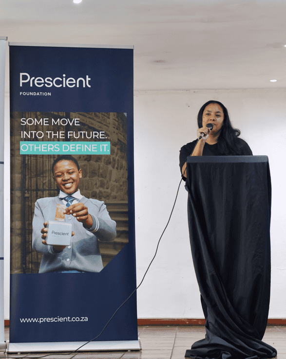 Woman speaking at a financial literacy event with Prescient Foundation banner in background.